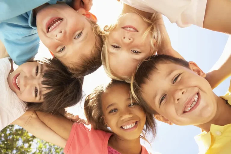 Five children laughing together in a circle, seen from below against a bright sky
