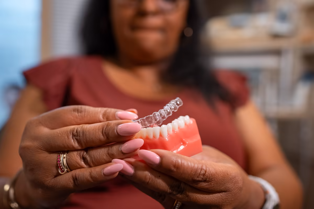 A patient holding a clear aligner on a dental model