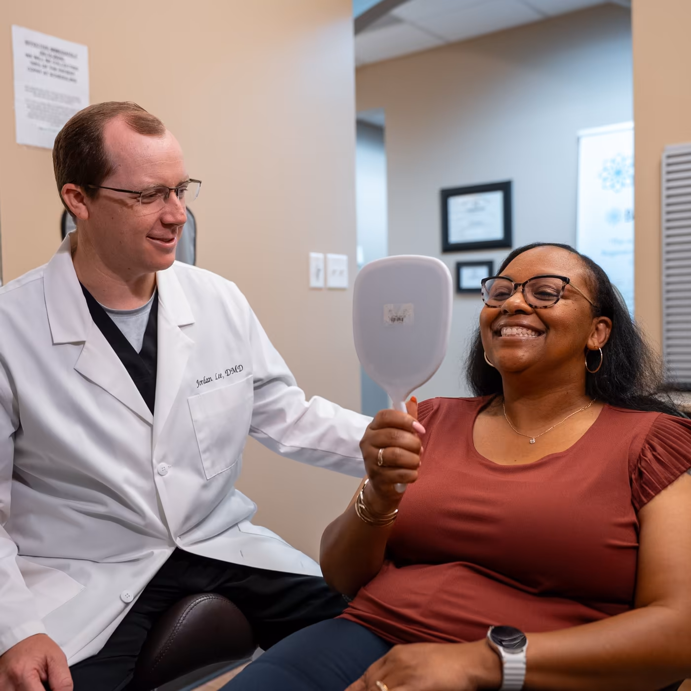 A patient checking her smile in a hand mirror beside Dr. Jordan Lee at Smiles of Cary