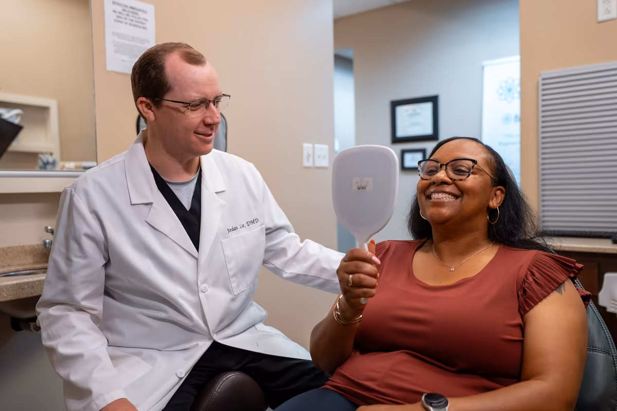 A patient checking her smile in a hand mirror beside Dr. Jordan Lee at Smiles of Cary