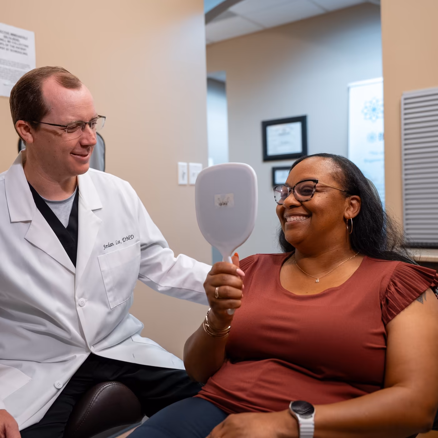 A patient smiling into a hand mirror as Dr. Jordan Lee looks on at Smiles of Cary